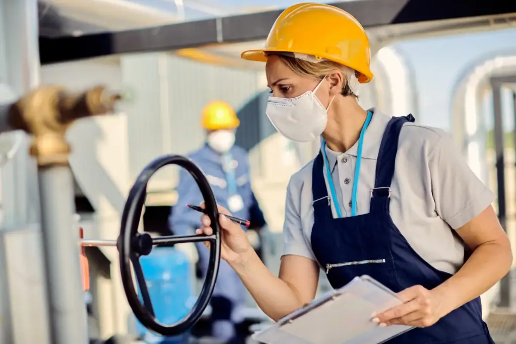 female-inspector-with-face-mask-examining-machine-valve-outdoor-industrial-facility